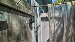 A laundry area with a metal rack, a hanging shower curtain, and a wooden wall with a sign. - Vineyard Gem < 2 Mi to Beach & Oak Bluffs! (Oak Bluffs)