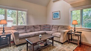A living room with a brown sofa, a coffee table, two lamps, a framed picture on the wall, and a window with blinds. - Vineyard Gem < 2 Mi to Beach & Oak Bluffs! (Oak Bluffs)