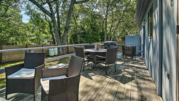 An outdoor deck with wicker furniture, a grill, and a view of trees and a house. - Vineyard Gem < 2 Mi to Beach & Oak Bluffs! (Oak Bluffs)