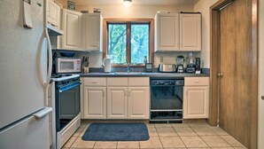 A kitchen with white cabinets, a microwave, an oven, a dishwasher, and a window with a view of trees. - Vineyard Gem < 2 Mi to Beach & Oak Bluffs! (Oak Bluffs)