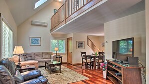 A spacious living room with a high ceiling, wooden flooring, a leather sofa, a dining area with a table and chairs, and a TV on a wooden stand. - Vineyard Gem < 2 Mi to Beach & Oak Bluffs! (Oak Bluffs)