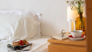 A neatly made bed with white linens, a bedside table with a book, a bowl, and a glass of water.