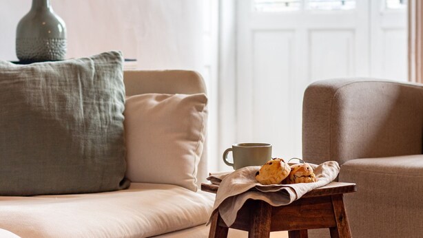 A cozy living room with a beige sofa, a wooden coffee table with a cloth, and a green vase.