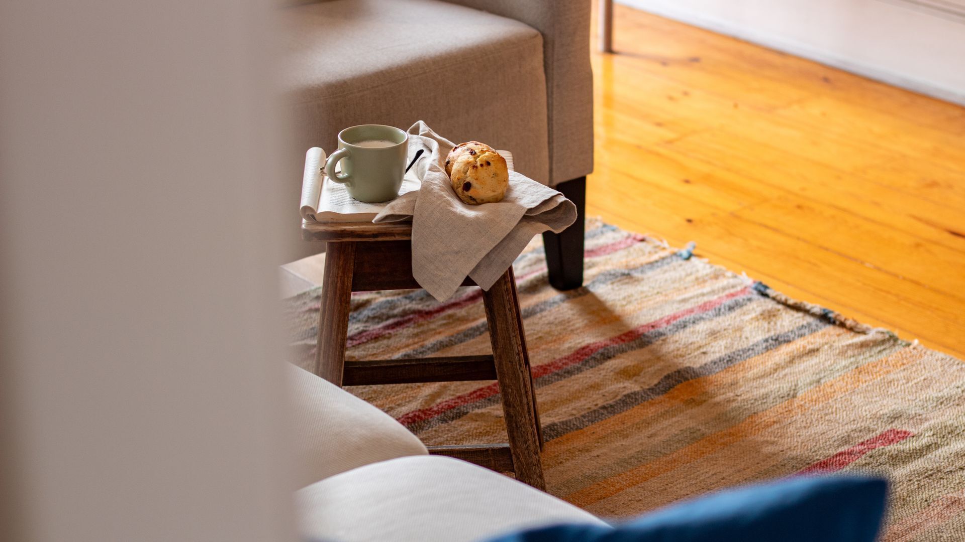 Una habitación acogedora con un taburete de madera, una taza y un muffin sobre una mesa.