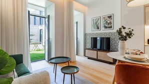 Una sala de estar moderna con un sofá, dos mesitas, un televisor y una zona de comedor con un florero.