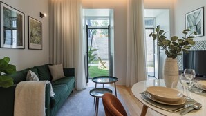 Una sala de estar con un sofá verde, una pequeña mesa redonda y un comedor con una mesa preparada para dos personas.