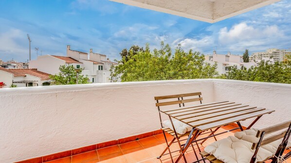 Eine Dachterrasse mit einer hölzernen Bank und einer Wäscheleine, mit Blick auf ein Wohngebiet mit weißen Gebäuden und grünen Bäumen.
