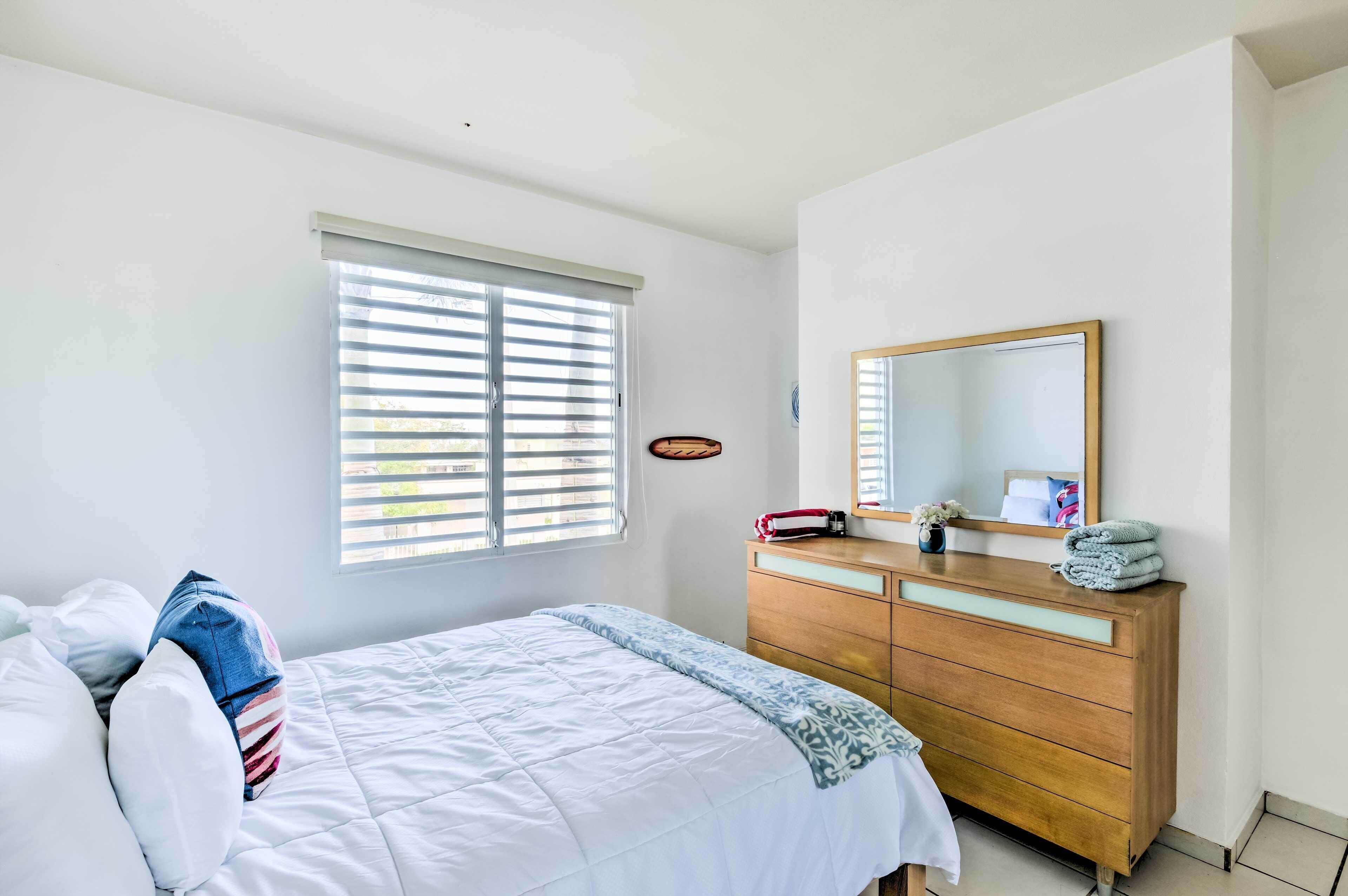 A bedroom with a bed, a dresser, a mirror, and a window with blinds.