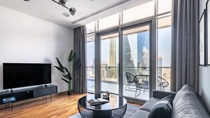Un soggiorno moderno con un'ampia televisione a schermo piatto, un tavolino rotondo, un divano e un balcone con vista sullo skyline cittadino.