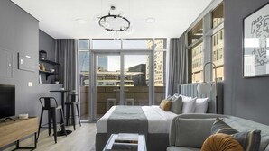 Una camera d'albergo moderna con un letto grande, un divano, un tavolino da caffè e una scrivania. Dalle ampie finestre si gode una vista sulla città.