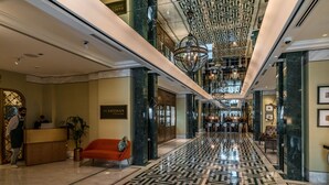 Un'accogliente hall d'albergo con pavimento in marmo, una reception, un divano rosso e un lampadario.