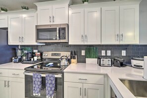 A modern kitchen with white cabinets, stainless steel appliances, and a black tiled backsplash. - Kissimmee Condo ~ 10 Mi to Disney Attractions (Kissimmee)