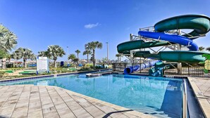 A pool with a water slide and palm trees in the background. - Kissimmee Condo ~ 10 Mi to Disney Attractions (Kissimmee)