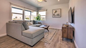 Uma sala de estar moderna com um sofá seccional cinza, uma pequena mesa lateral de madeira e uma grande janela com vista para a cidade.
