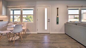 Uma sala moderna com um sofá cinzento, uma mesa de jantar com cadeiras e uma porta com uma faixa de luz vertical.