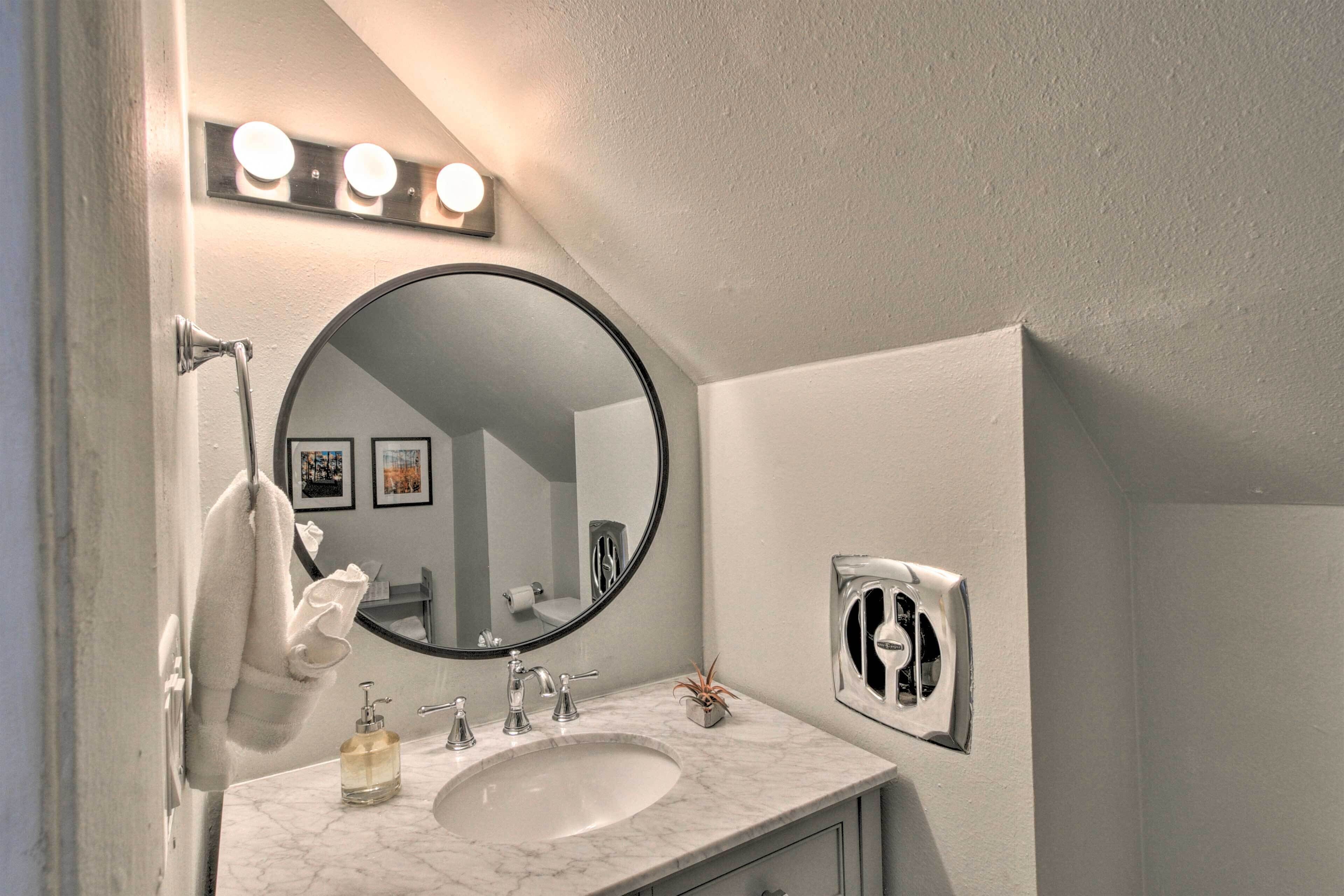 A bathroom with a white marble sink, a round mirror, and a towel hanging on the wall.