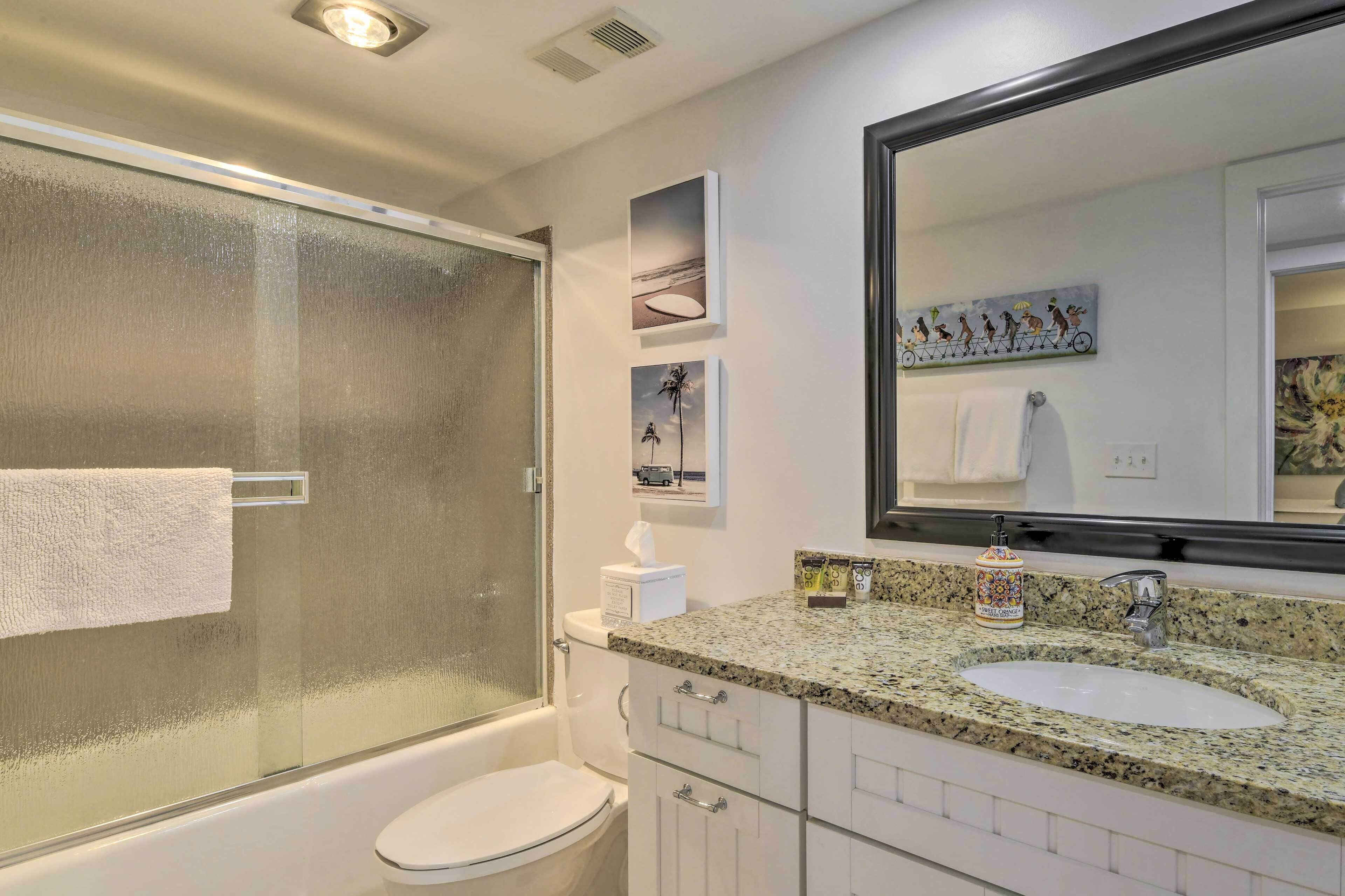 A modern bathroom with a glass-enclosed shower, a white toilet, a granite countertop sink, and a large mirror.