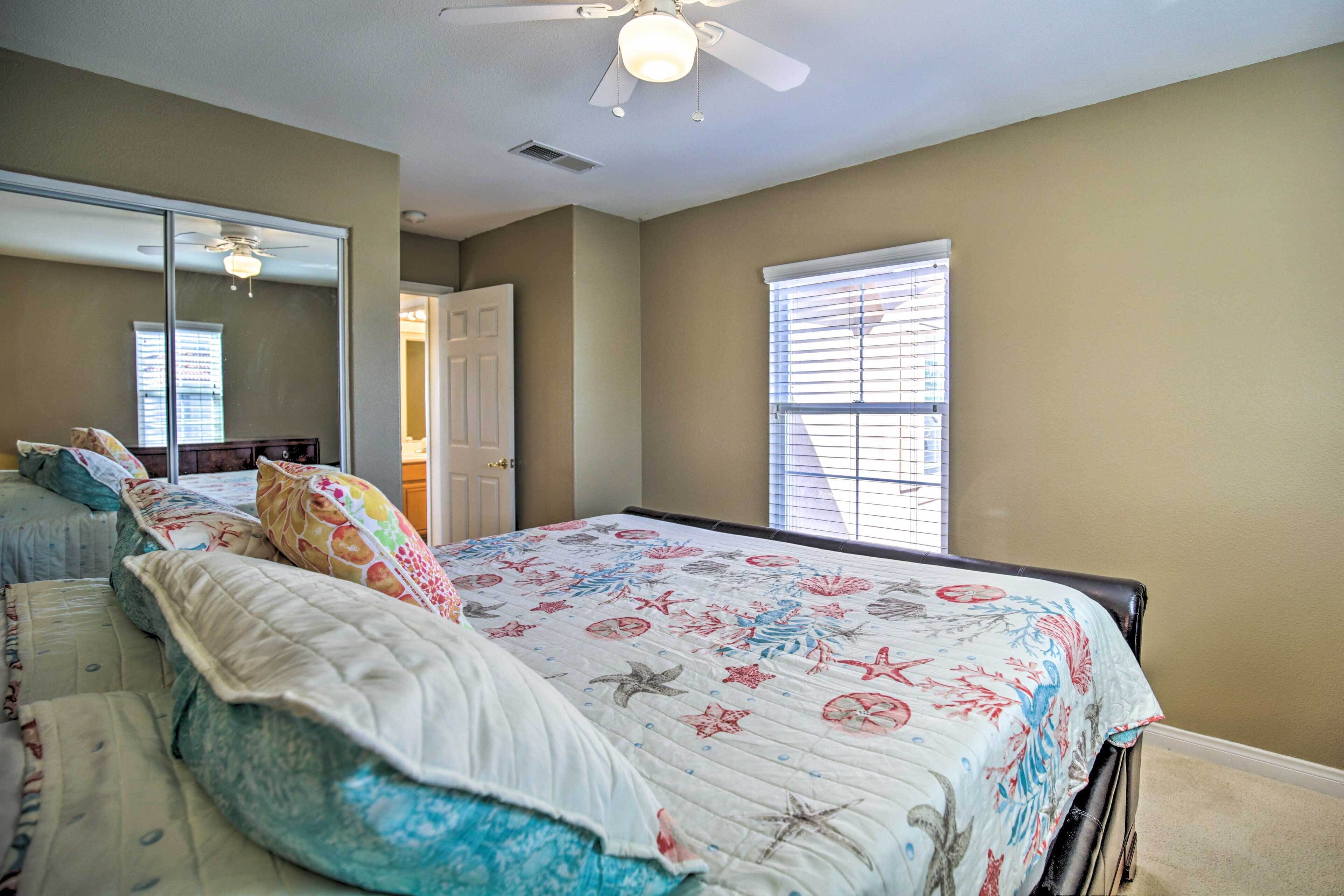 A bedroom with a bed, a ceiling fan, a window with blinds, and a door.