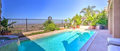 A swimming pool with a clear blue water, surrounded by a black metal fence, and potted plants.