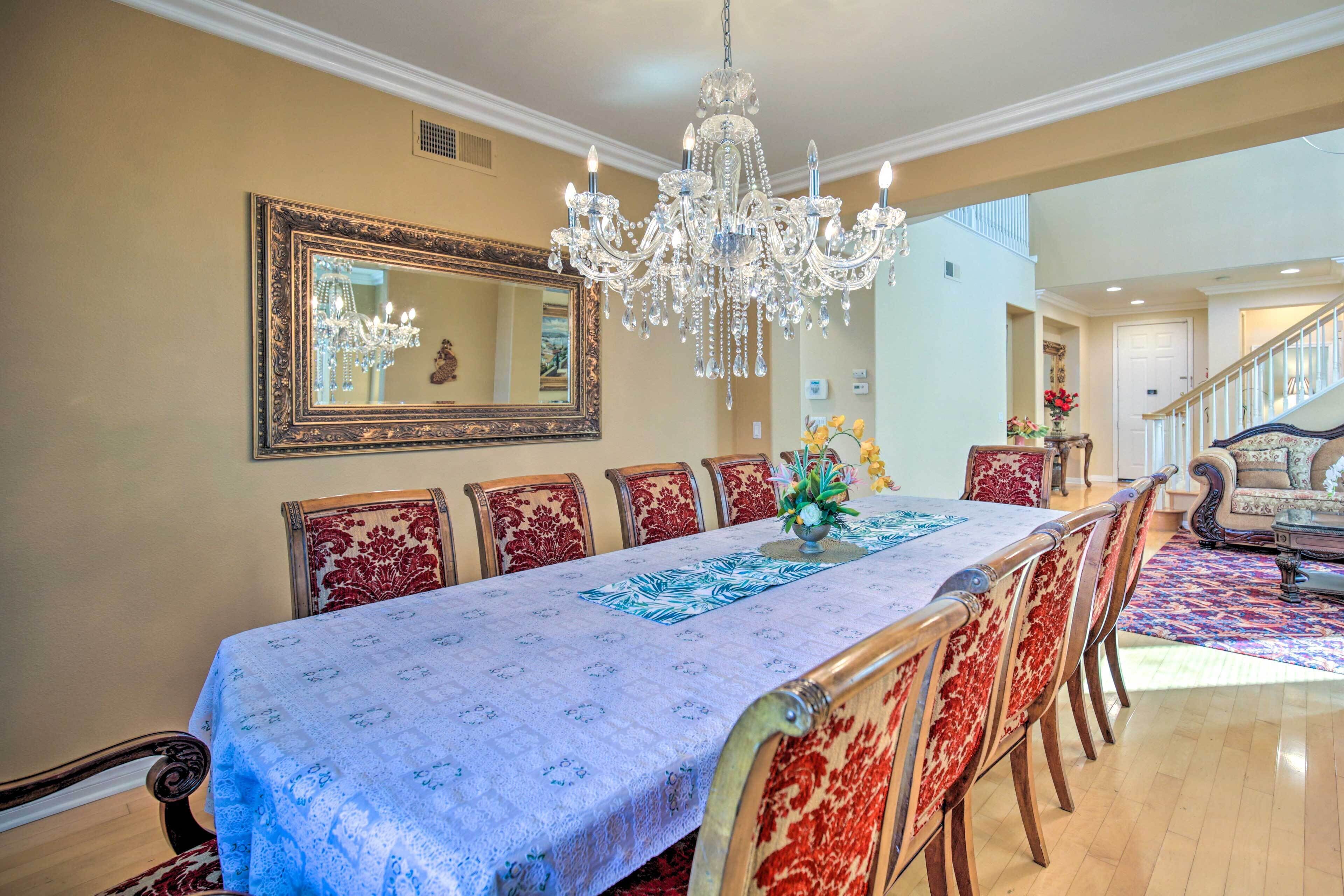 Comedor con una larga mesa, sillas ornamentadas, un candelabro y un espejo grande en la pared.