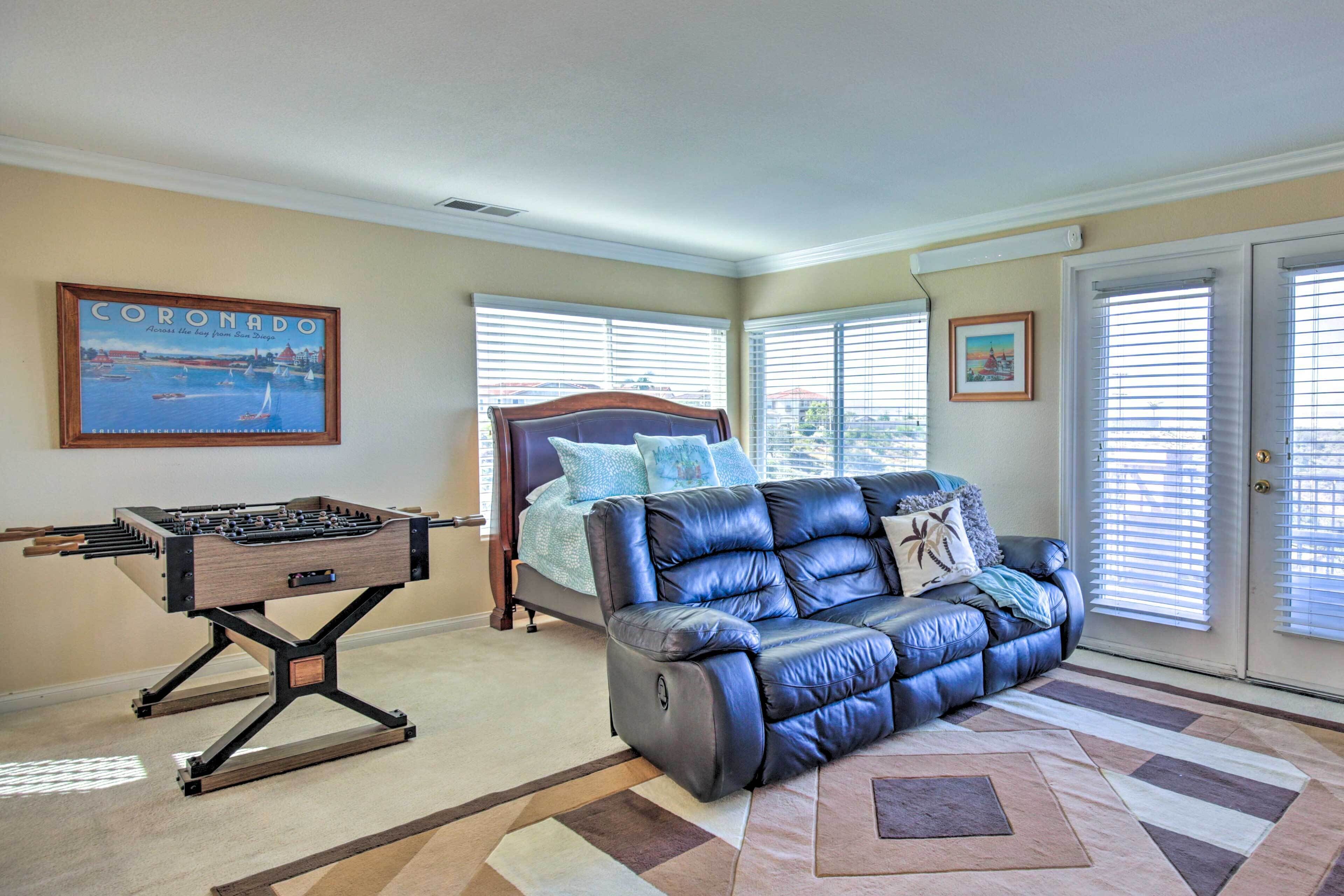 A living room with a foosball table, a blue leather sofa, a bed with a headboard, and a painting of Coronado.