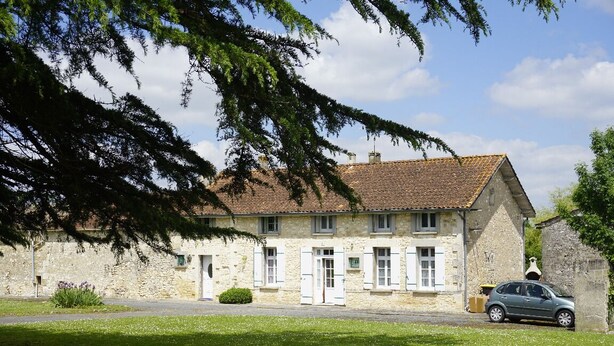 Un bâtiment en pierre avec un toit recouvert de tuiles, une voiture garée devant et une pelouse bien entretenue.