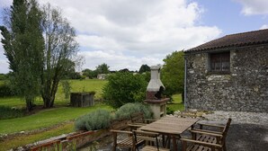 Un espace de restauration en plein air au style rustique, avec un bâtiment en pierre, une table et des chaises en bois, et une cheminée.