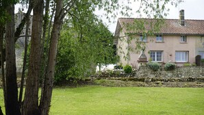 Une maison avec un mur en pierre, une pelouse verdoyante et des arbres.