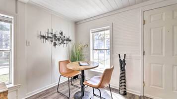 A dining area with a round wooden table and two chairs, a decorative wall piece, and a door with a coat rack beside it.