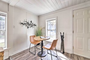 A dining area with a round wooden table and two chairs, a decorative wall piece, and a door with a coat rack beside it. - Idyllic Fayetteville Home - Walk to UA Campus! (Fayetteville)