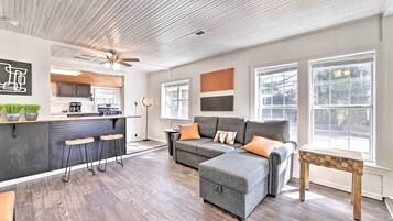 A modern living room with a gray sectional sofa, a wooden coffee table, and a kitchen area with a bar counter and stools.