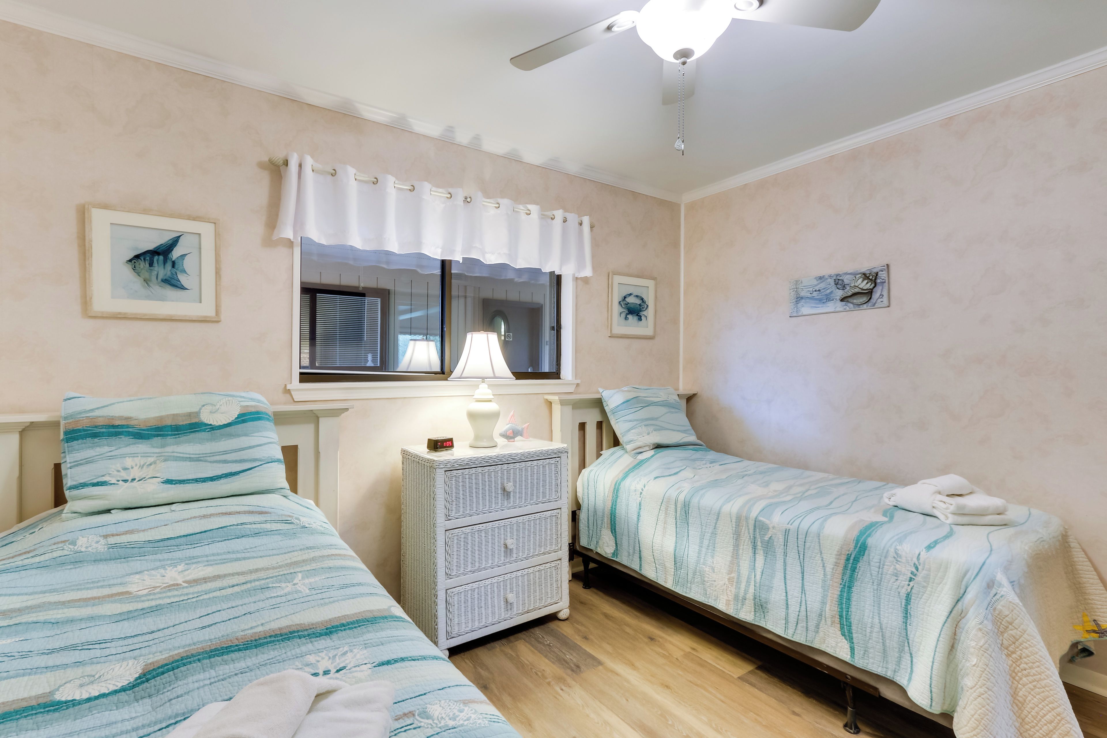A bedroom with two beds, a nightstand, a window with curtains, and wall art.
