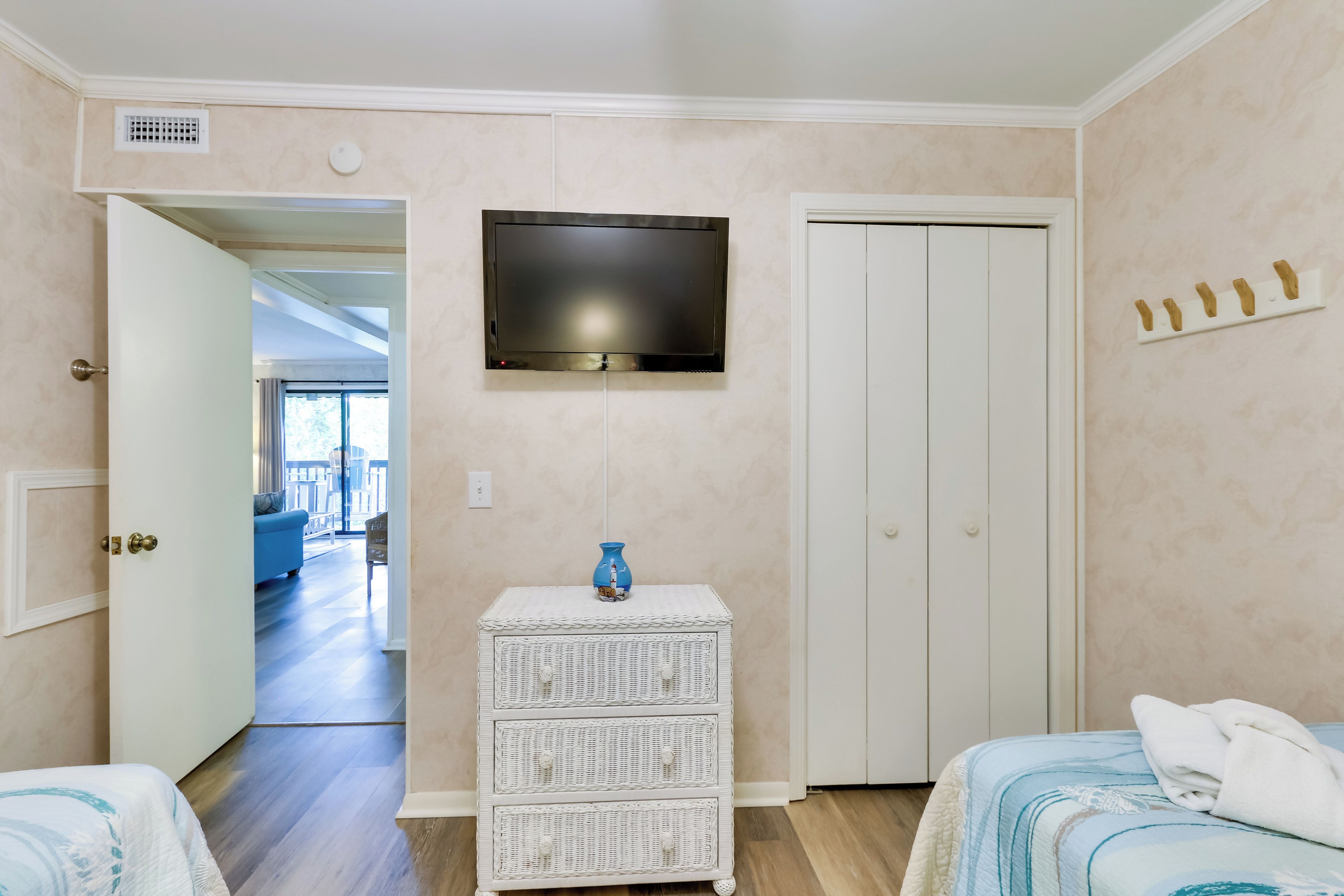 Un dormitorio con una televisión instalada en la pared, un aparador blanco y una cama con colcha de diseño azul y blanco.