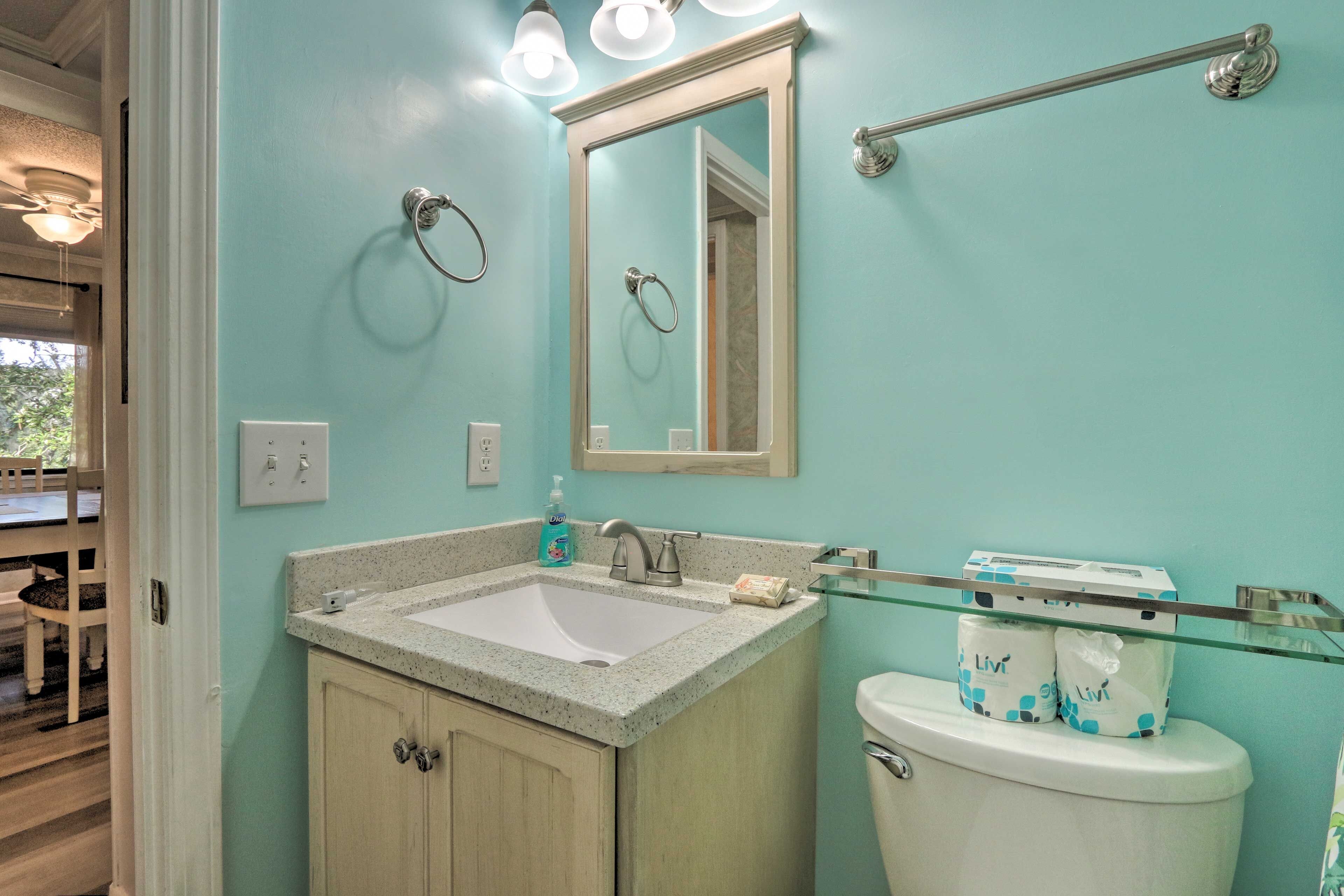 A bathroom with a sink, mirror, and toilet. There are two rolls of toilet paper on the toilet.