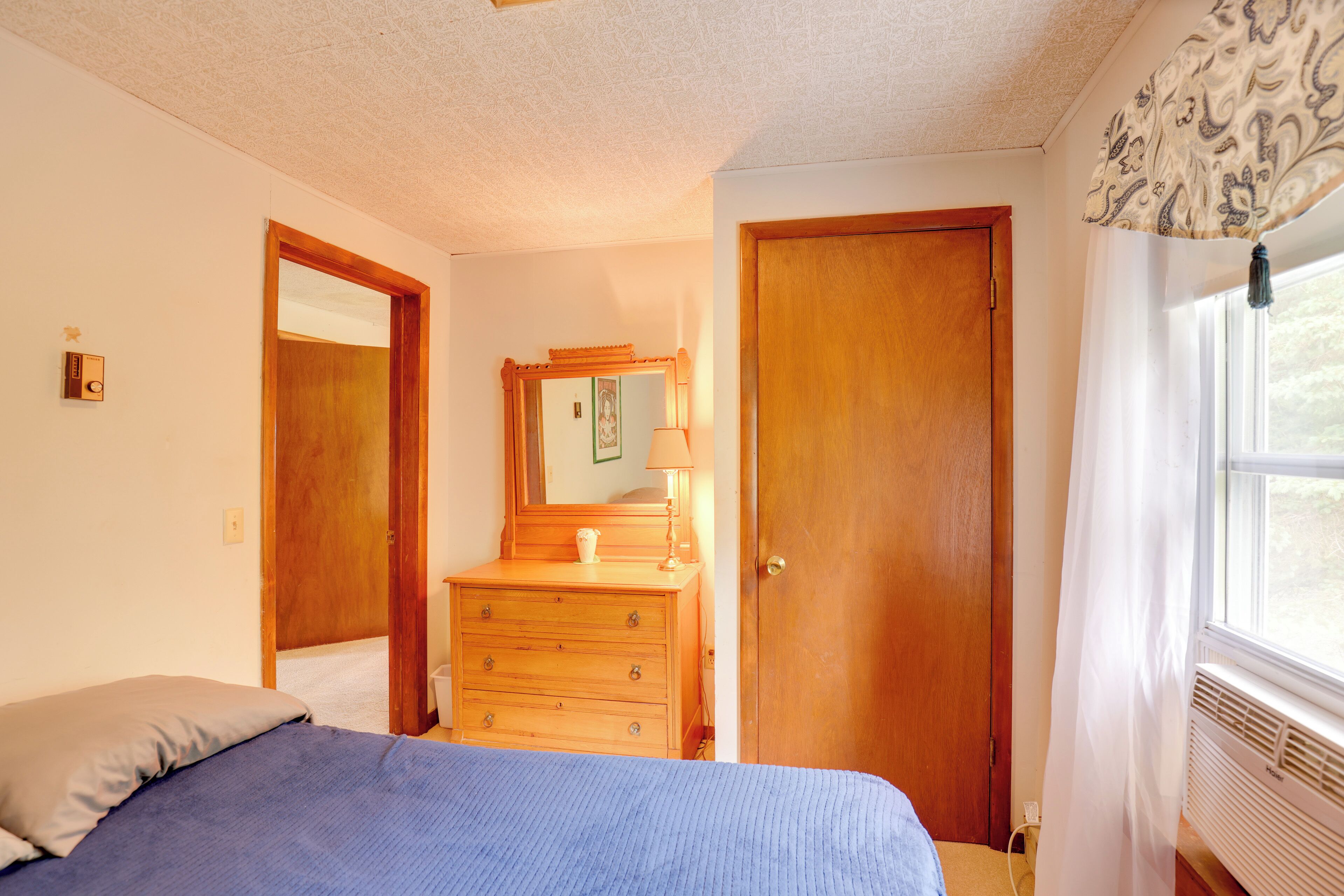 A bedroom with a bed, dresser, mirror, and a window with curtains.