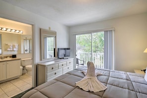 A hotel room with a bed, a television, a bathroom with a toilet and sink, and a balcony with a view of greenery. - Cozy Kissimmee Townhome ~ 8 Mi to Disney World! (Kissimmee)