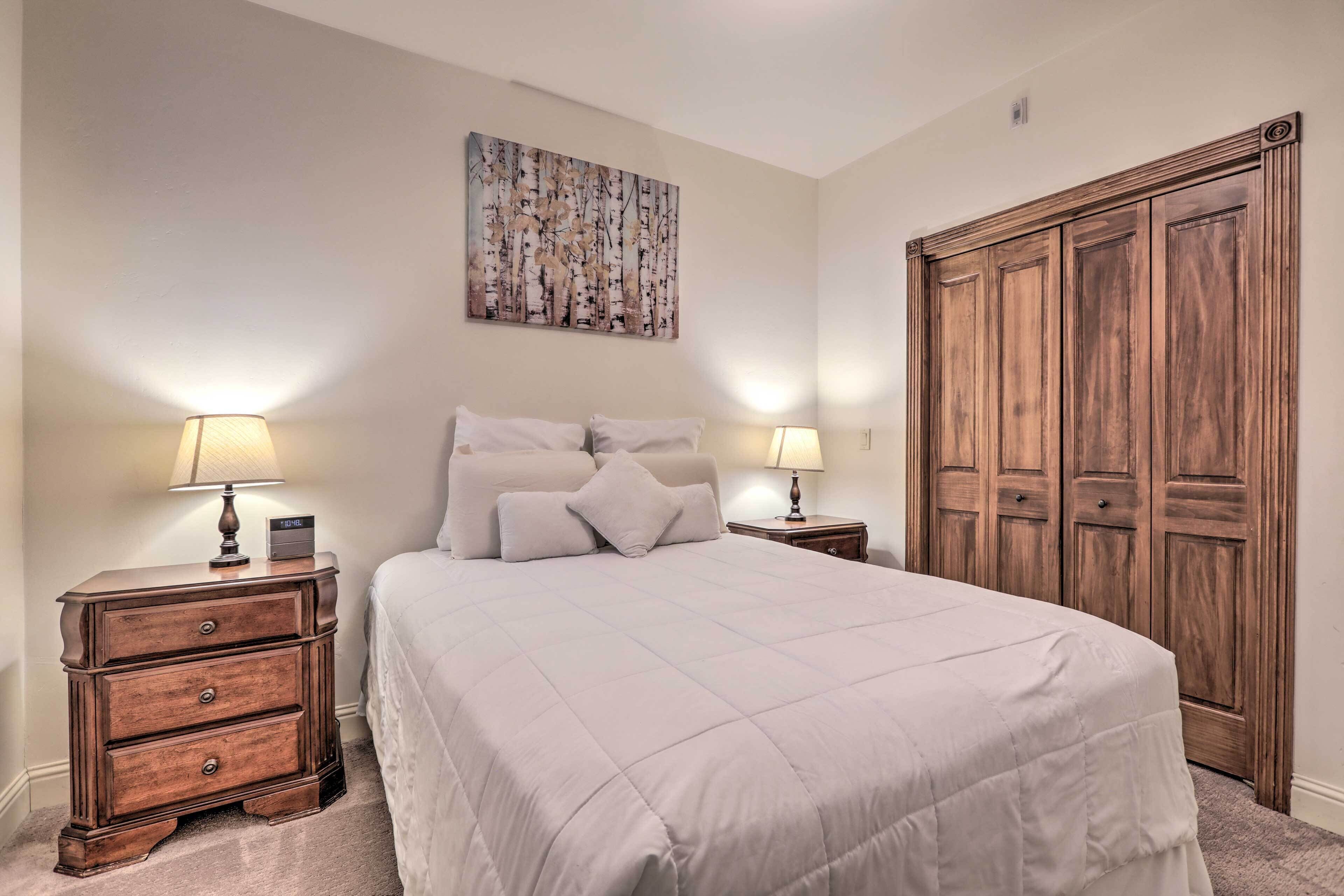 A neatly arranged bedroom with a large bed, two bedside tables with lamps, a wooden wardrobe, and a wall-mounted painting.