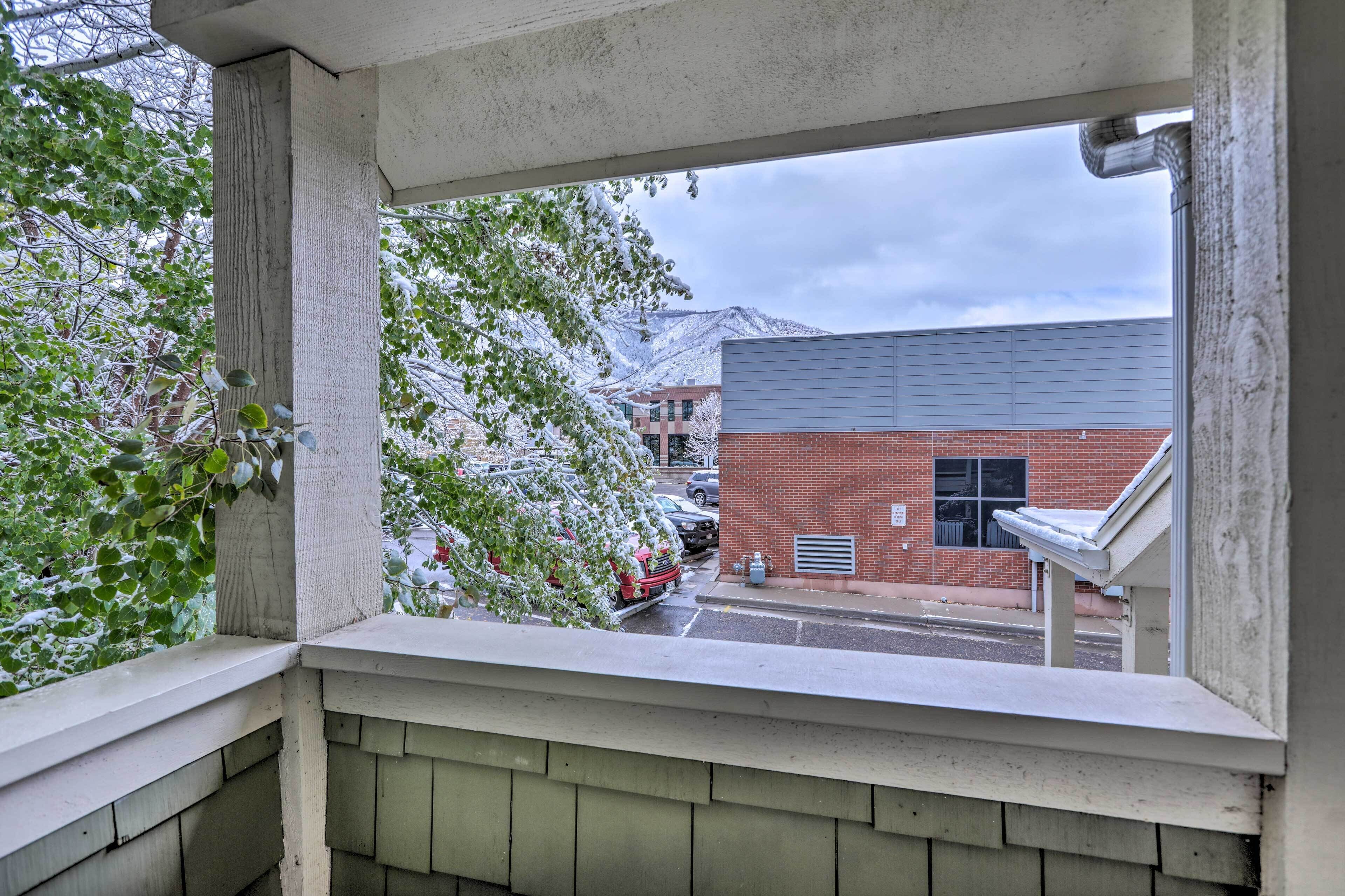 A view from a balcony with a snow-covered tree and a brick building in the background.