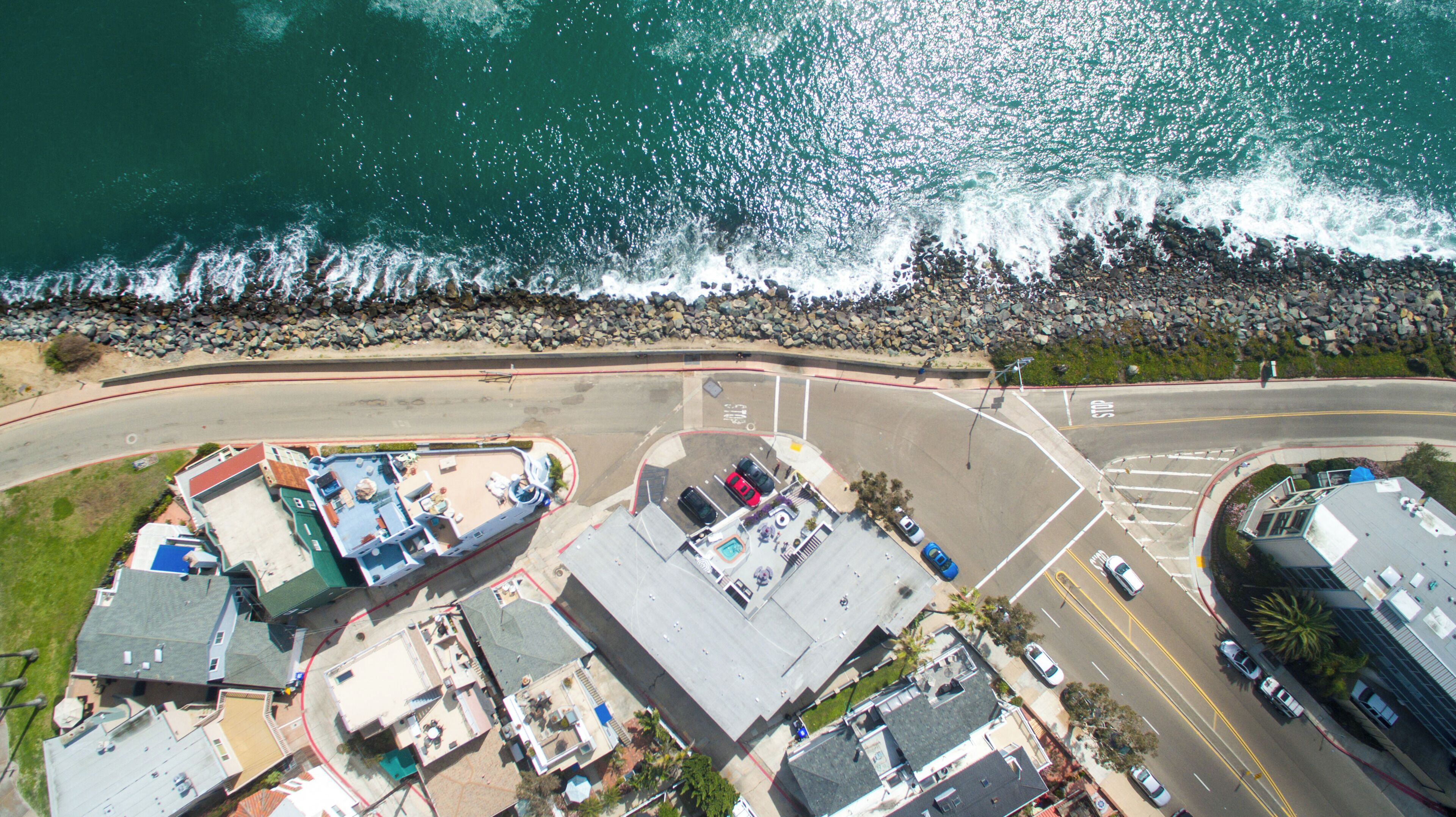 An aerial view of a coastal area with a parking lot, buildings, and a rocky shoreline.