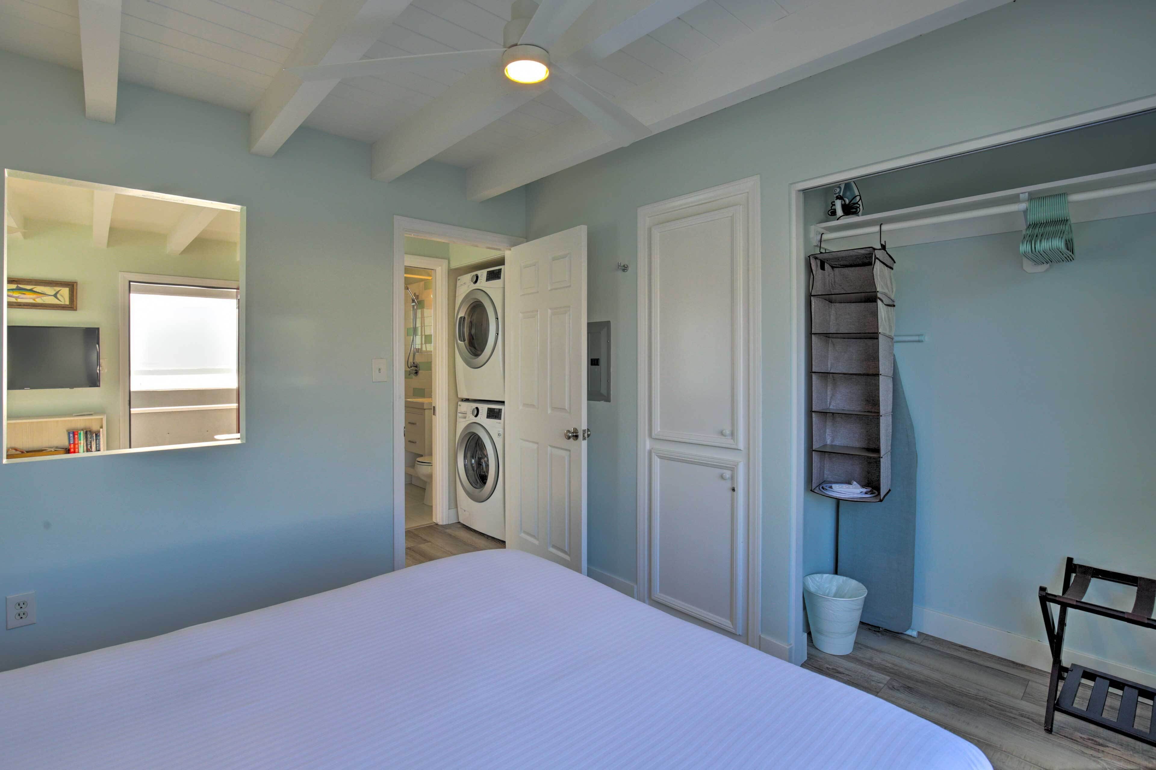 A bedroom with a bed, a washing machine, a mirror, and a wardrobe.