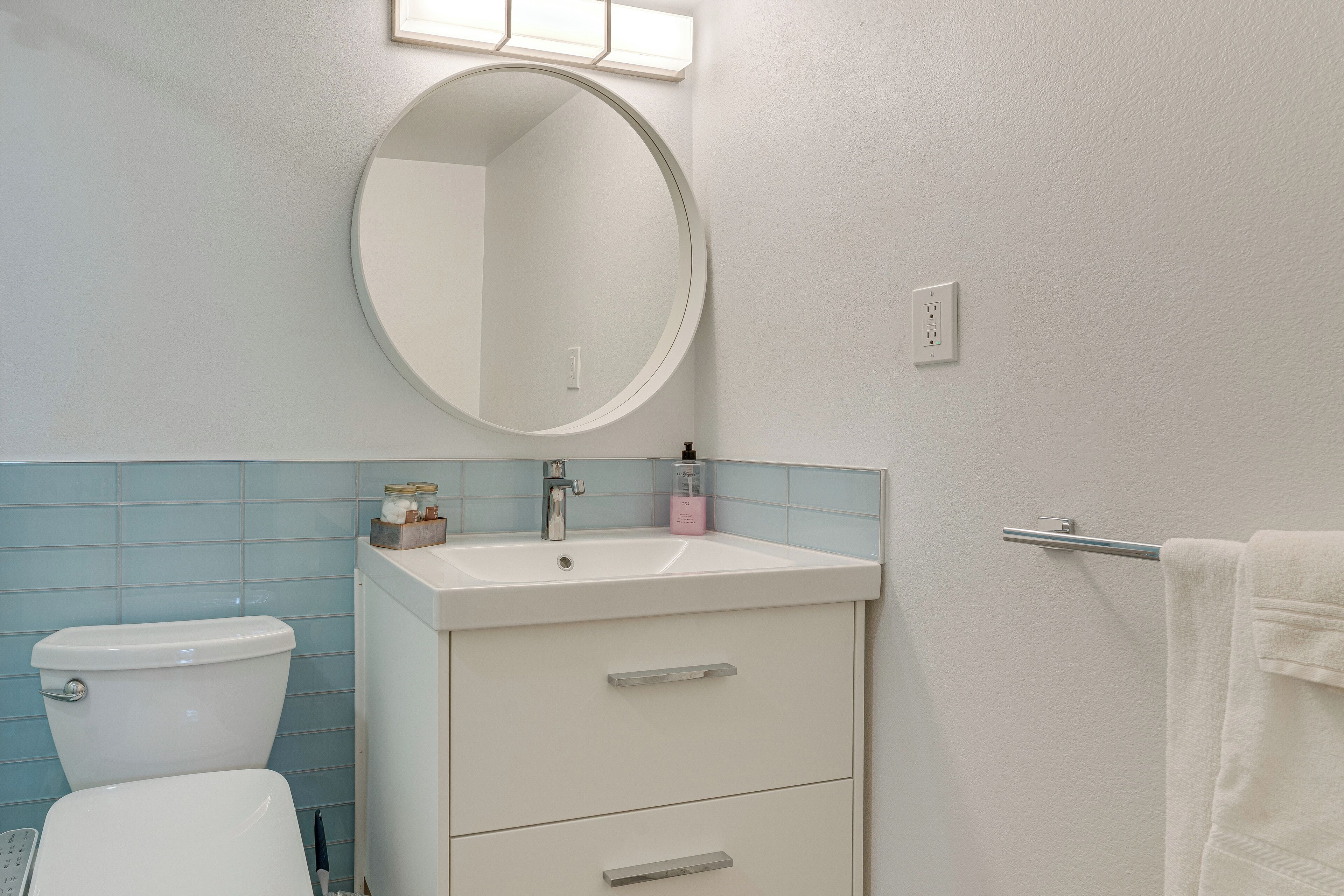 A bathroom with a toilet, sink, mirror, and towel rack.