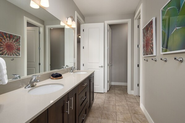 A modern bathroom with two sinks, a large mirror, and a door leading to another room.