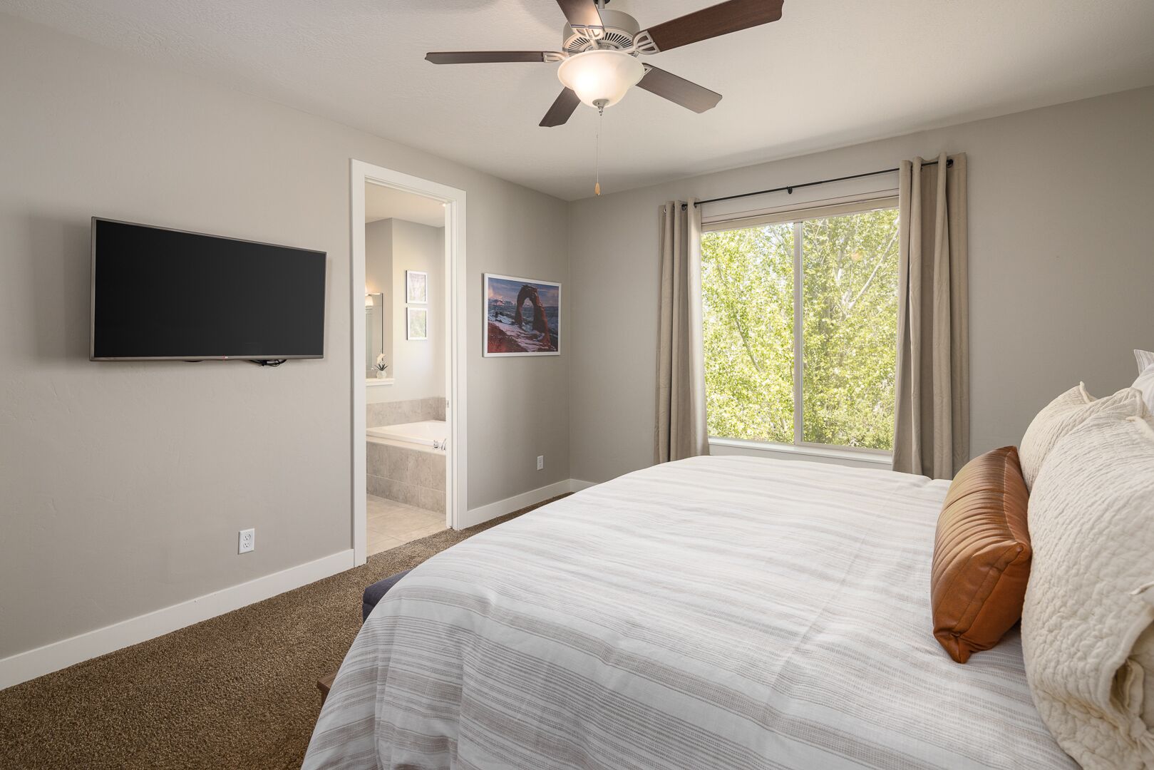A bedroom with a bed, a ceiling fan, a TV, and a window with curtains.