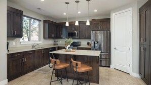 Una cocina moderna con armarios de madera oscura, electrodomésticos de acero inoxidable y una isla central con taburetes de bar.