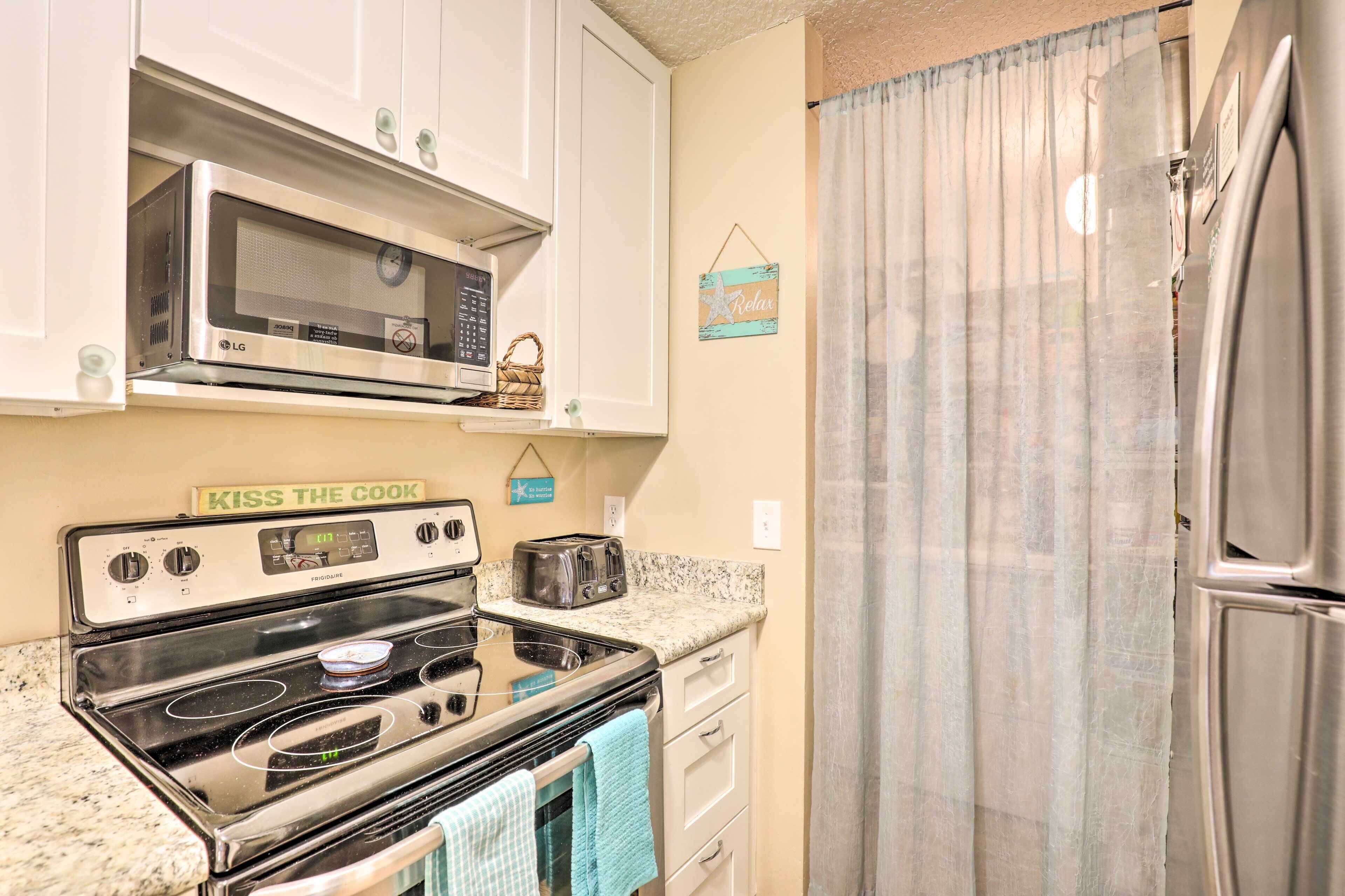 A kitchen with a stainless steel stove, microwave, and refrigerator. There is a 'KISS THE COOK' sign above the stove.