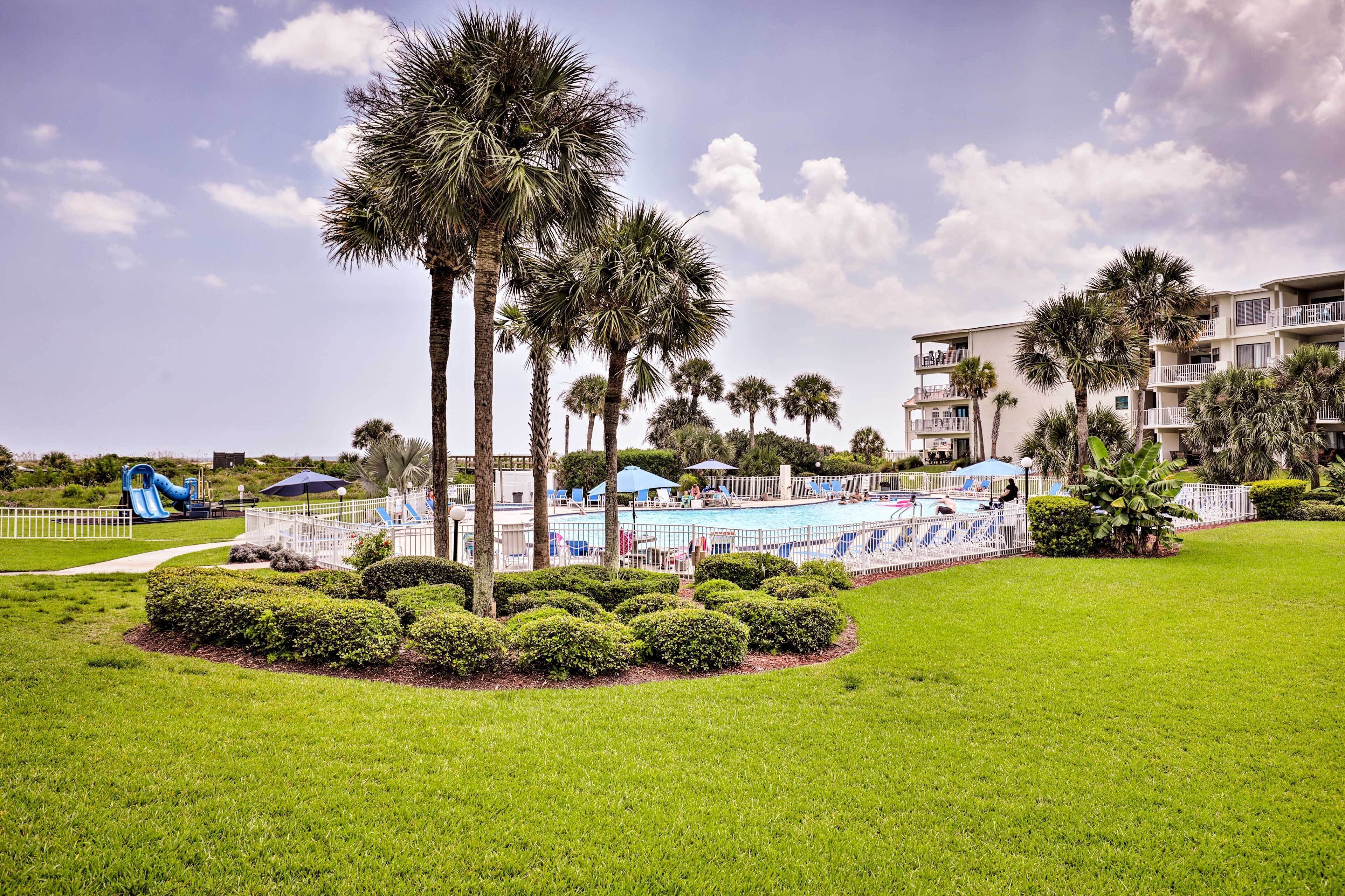 A resort with a swimming pool, palm trees, and a playground.
