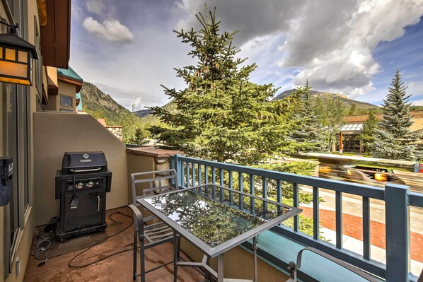A balcony with a glass table and chairs, a barbecue grill, and a view of a mountain and trees. - 7 Mi to Skiing: Main St Frisco Condo w/ Balcony! (Frisco)