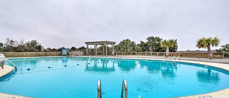 Una piscina azul cristalina con dos escaleras metálicas al frente, rodeada de palmeras y una cerca de madera.