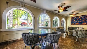 A dining area with a round table and four upholstered chairs, large arched windows with metal bars, and ceiling fans. - Luxurious San Juan Villa w/ Pool - Walk to Beach! (San Juan)