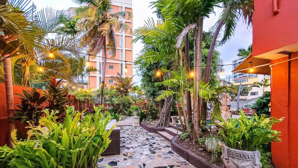 A pathway with potted plants and string lights, leading to a building with a red exterior. - Luxurious San Juan Villa w/ Pool - Walk to Beach! (San Juan)